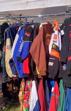 many shirts are hanging up on the clothes rack at an outdoor flea market in front of a tent