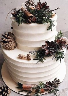 a three tiered white cake with pine cones and greenery on the top layer