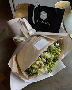 a bouquet of flowers is wrapped in paper and sitting on a table next to a chanel bag