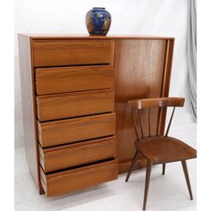 a wooden dresser sitting next to a chair and vase on it's top shelf