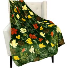 a green blanket with yellow and red flowers on it is sitting in a white chair