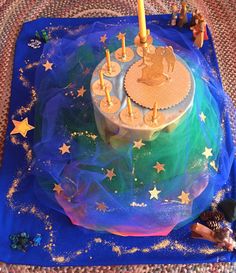 a birthday cake with candles and stars on the blue tablecloth, surrounded by small figurines