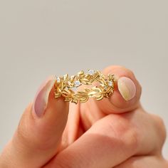 a woman's hand holding a gold ring with leaves on the middle and sides