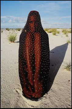 a woman standing in the sand with her back turned to the camera, wearing a black and white polka dot dress