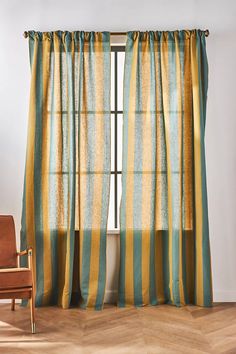 a chair sitting in front of a window with curtains on top of it and a striped curtain