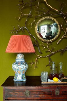 a table with a lamp, vase and mirror on it next to a wall decoration