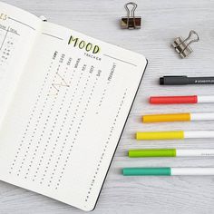 an open notebook next to several pens and a clipboard with the word mood written on it