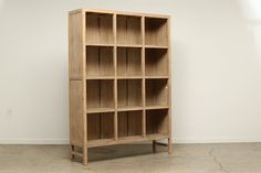 a wooden bookcase sitting on top of a cement floor next to a white wall