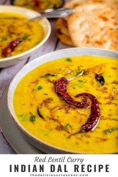 red lentil curry in a white bowl on a table with bread and spoons