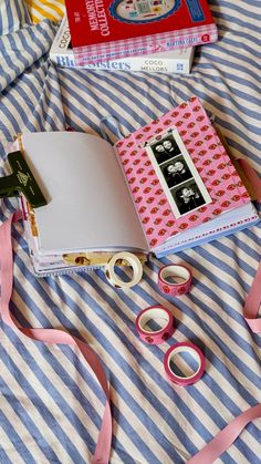 there is a book, pair of scissors and tape on top of a bed with striped sheets