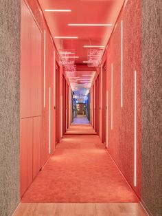 a long hallway with red walls and wooden floors is lit by neon lights on the ceiling