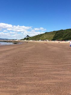 people are walking along the beach on a sunny day with blue skies and white clouds