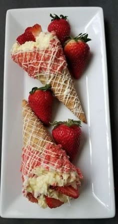 some strawberries are on a white plate and one is cut in half to look like an ice cream sundae