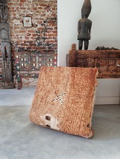 two pieces of woven material sit on the floor in front of a brick wall and sculpture