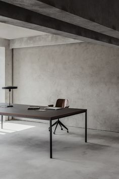 an empty room with a table and two lamps on the floor, in front of a concrete wall