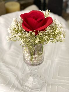 a red rose in a clear glass vase filled with white flowers and baby's breath