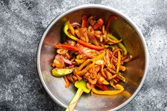 a bowl filled with meat and vegetables on top of a gray countertop next to a wooden spoon