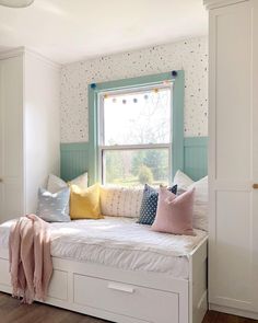 a white daybed with colorful pillows and blankets on it in front of a window