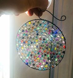 a hand holding a circular glass ornament with multicolored beads