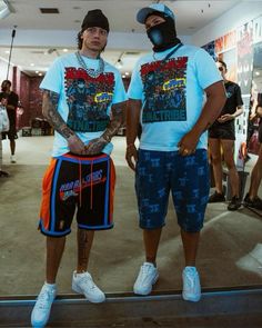 two men standing next to each other in shorts and t - shirts with tattoos on their arms