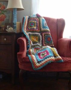 a crocheted granny blanket sitting on top of a chair next to a lamp