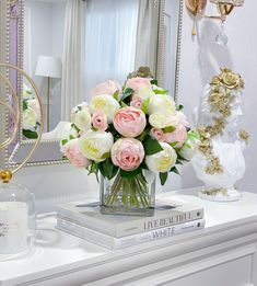 a vase filled with pink and white flowers sitting on top of a dresser next to a mirror