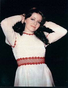 a woman in a white and red dress posing for the camera with her hands on her head