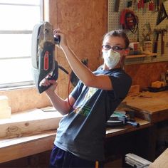 a woman wearing a mask and holding a circular saw in her hands while standing next to a workbench