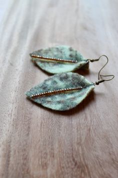 two green leaf shaped earrings sitting on top of a wooden table