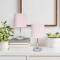 two pink lamps sitting on top of a white dresser next to a mirror and potted plant