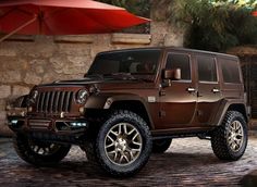 a brown jeep parked in front of a stone wall with an umbrella over it's head