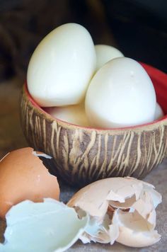 three eggs are in a bowl next to an egg shell and one is broken open