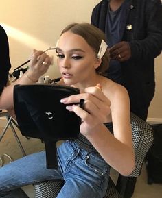 a woman getting her make up done in front of a man who is sitting down