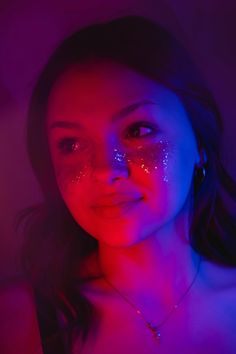 a young woman with glitter on her face and chest posing for a photo in the dark