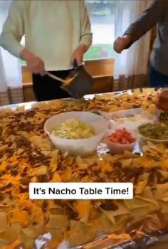 two people standing over a table with food on it and one person holding a knife