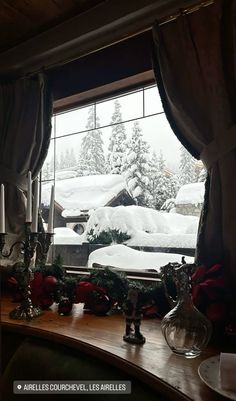 a table with candles and christmas decorations on it in front of a snow covered window