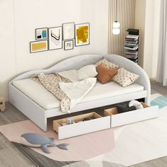 a white bed sitting on top of a wooden floor next to a wall with pictures above it