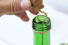 a person is holding a cork in front of a green water bottle with a gold ring on it