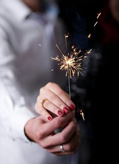 a woman holding a sparkler in her hand with red nail polishes on it