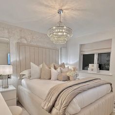 a large white bed sitting in a bedroom next to a window with a chandelier above it