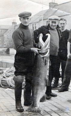 an old black and white photo of men holding up a fish in front of them