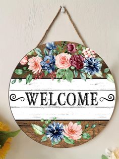 a welcome sign hanging from the side of a wall with flowers and leaves on it