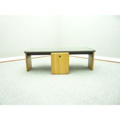 a wooden table with a black top and yellow legs on carpeted floor in front of white wall