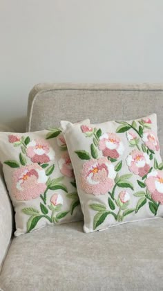 two pillows sitting on top of a couch in front of a white wall with flowers