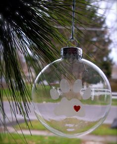 a glass ornament with a dog's paw and heart on it hanging from a pine tree