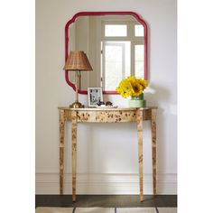 a mirror sitting on top of a table next to a lamp and vase with flowers