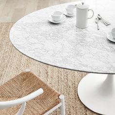 a white table with two cups and saucers on it, next to a wicker chair