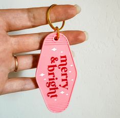 a hand holding a pink keychain with merry written in red on the front