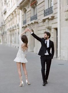 a man and woman in formal wear walking down the street with their arms up to each other