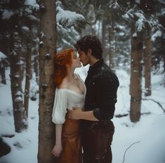 a man and woman standing next to each other in front of snow covered forest trees